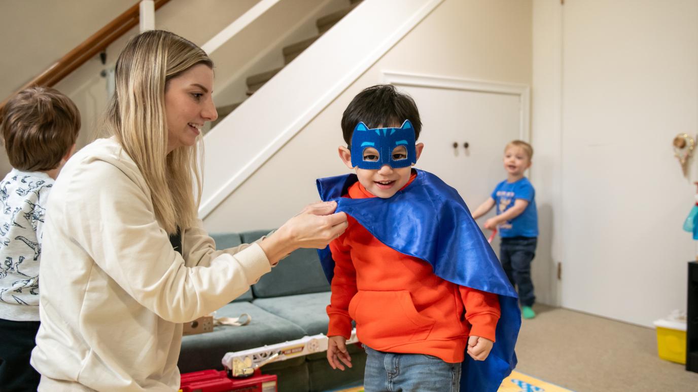 Child Care provider helping young boy dress up as a super hero
