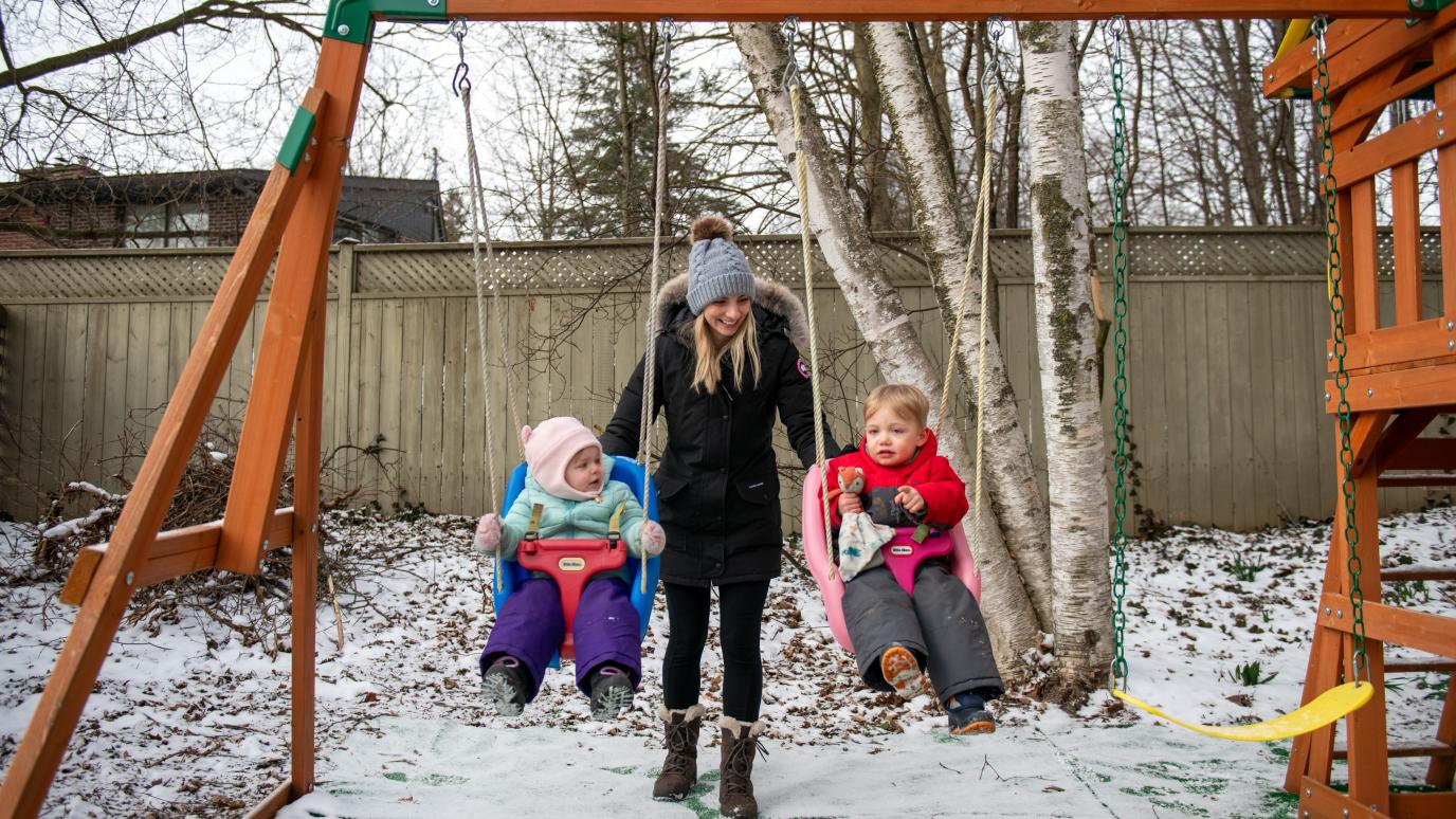 Child Care provider pushing two kids on swings.