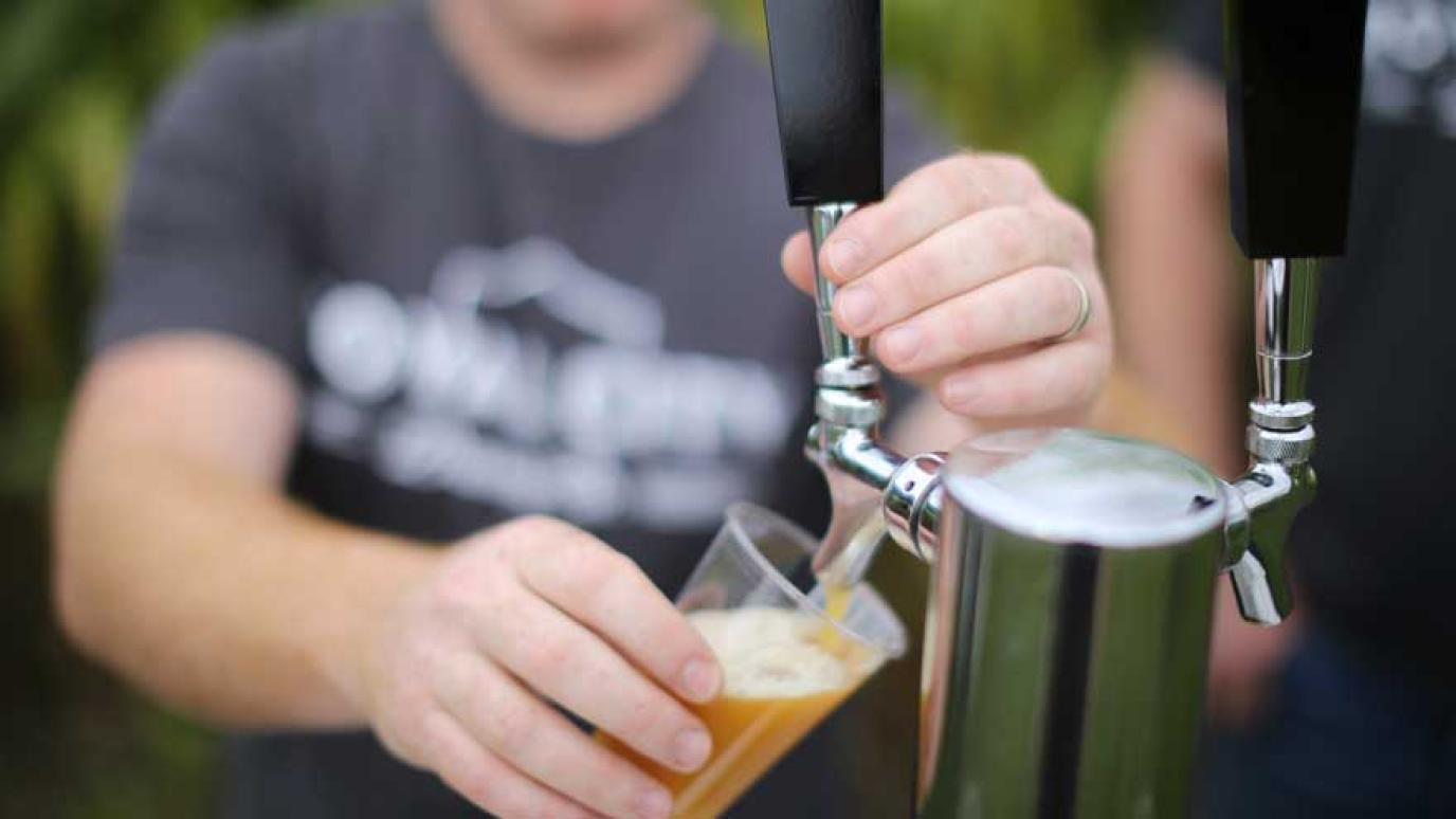 Man pouring beer into a glass from a draught tap at an outdoor event