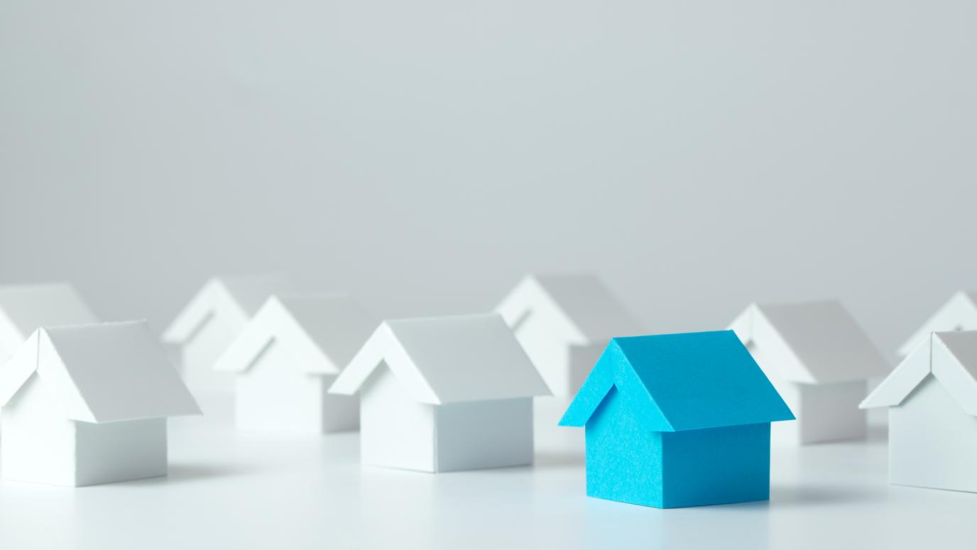 A blue paper house in a row of white paper houses