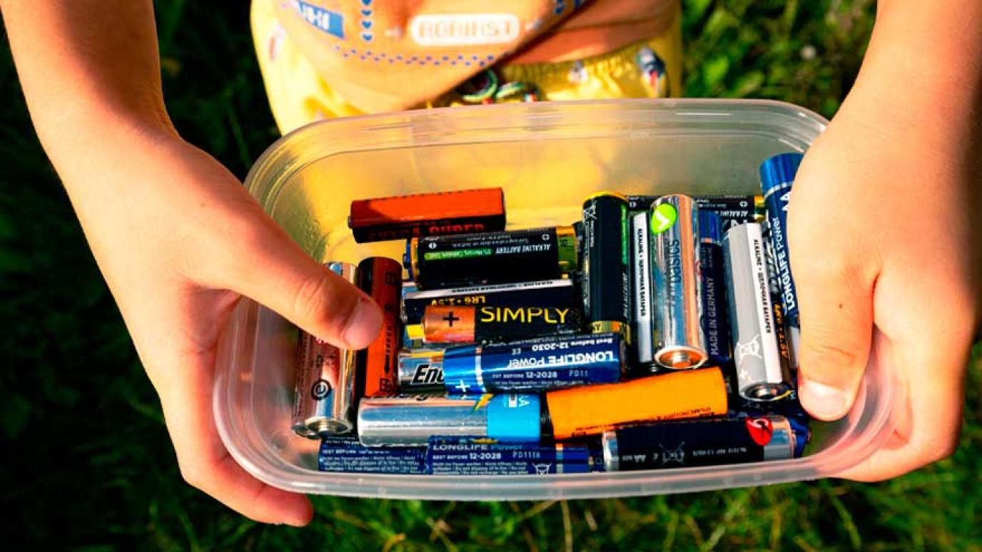 Child holding a tupperware filled with used batteries ready for disposal