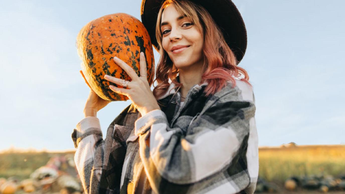 Young hipster woman, wearing a plaid shirt, holds up a pumpkin at a pumpkin patch.