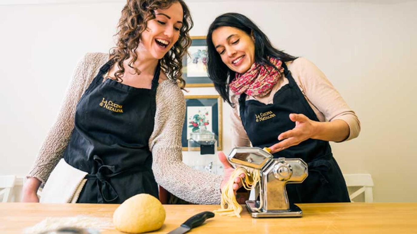 Two woman having fun making fresh pasta with a pasta press