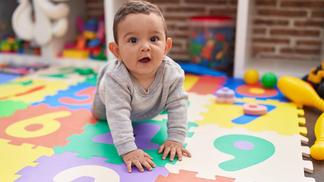 Adorable baby crawling on coloured floor mat in a child care setting