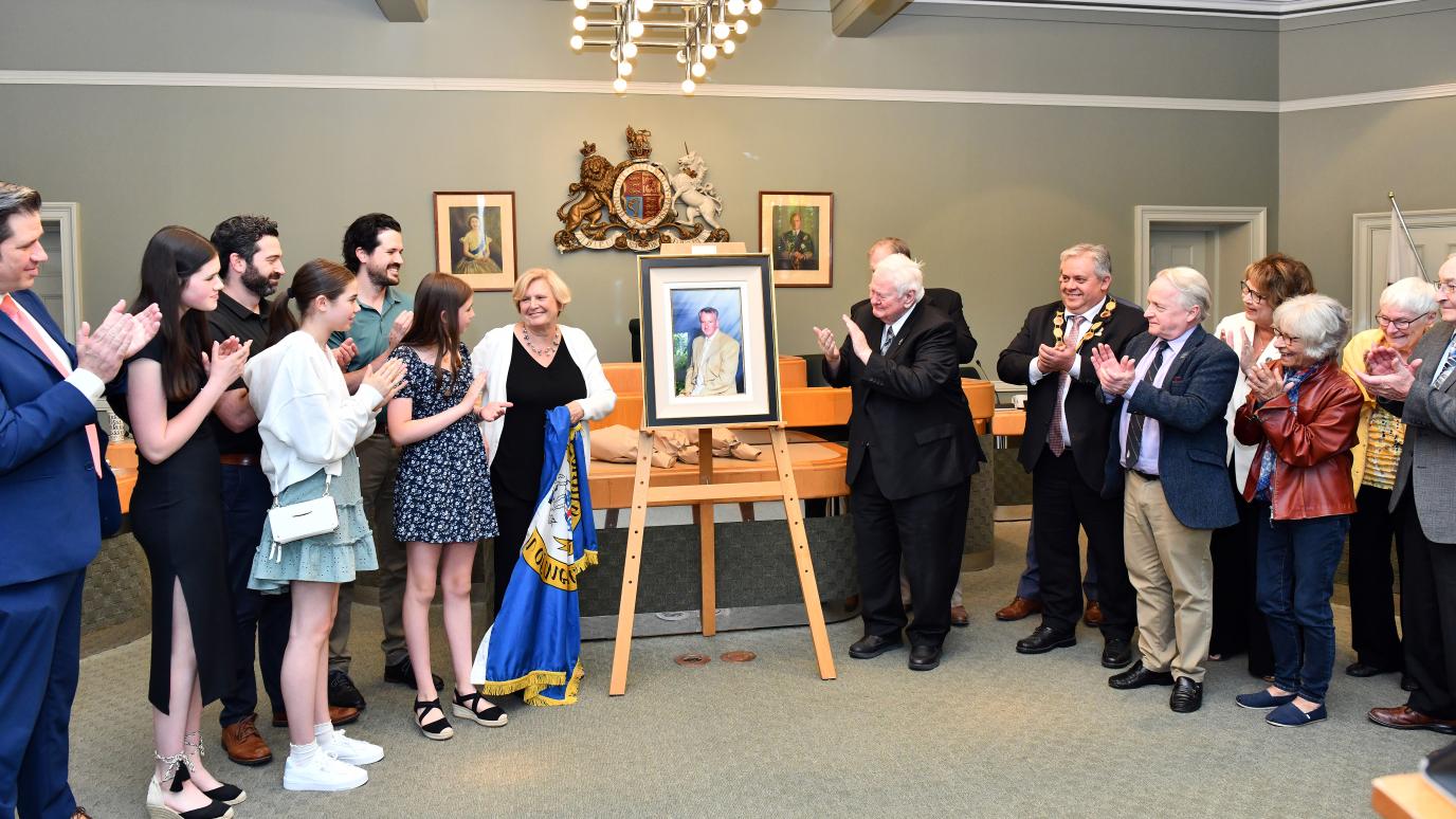 People stand on either side of an unveiled portrait of past Warden, Jim Andrews. 
