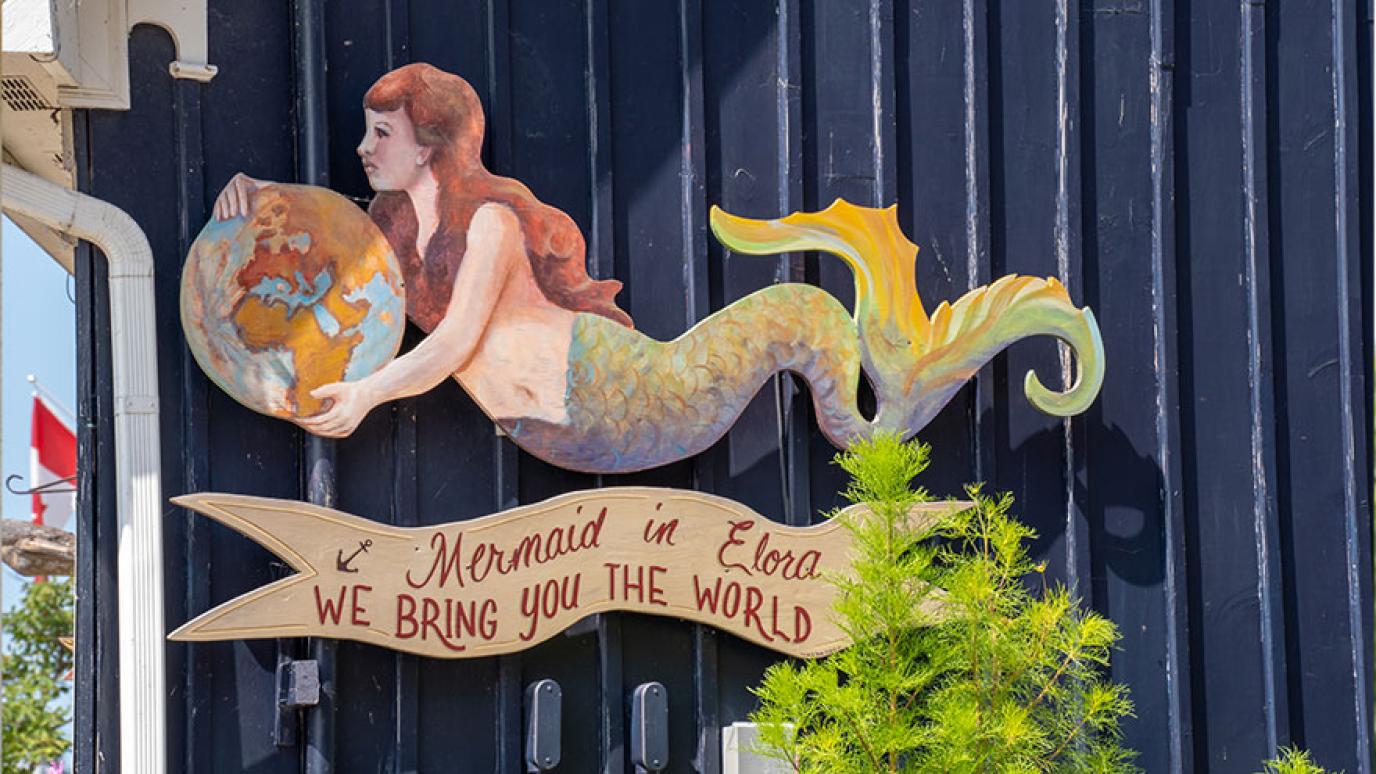 A wooden cut out Mermaid sign marks a store entrance 