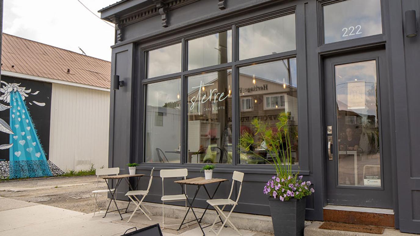 The modern interior of a gift shop and cafe with large front windows and a table and chairs out front. 