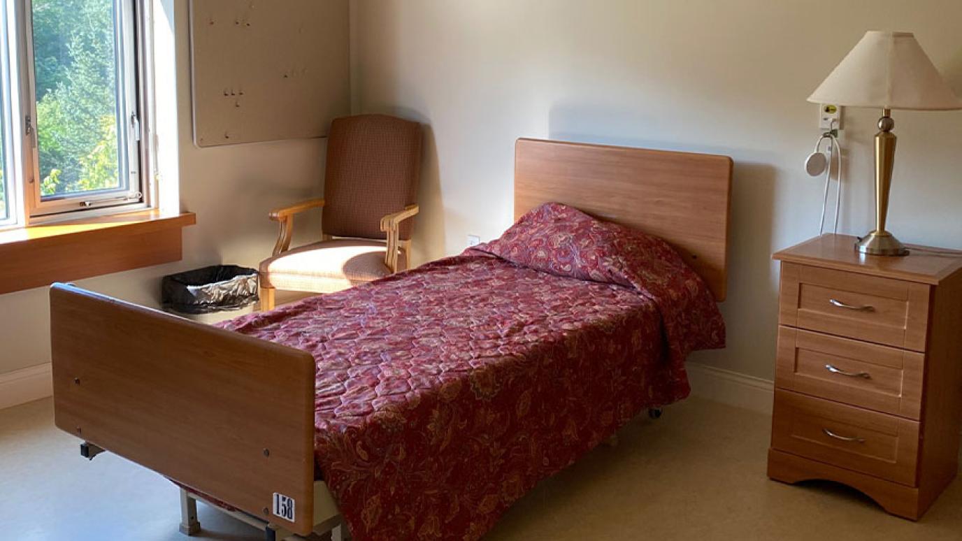 Single room with a bed, side table and lamp, bedside chair, and lovely garden view from the window