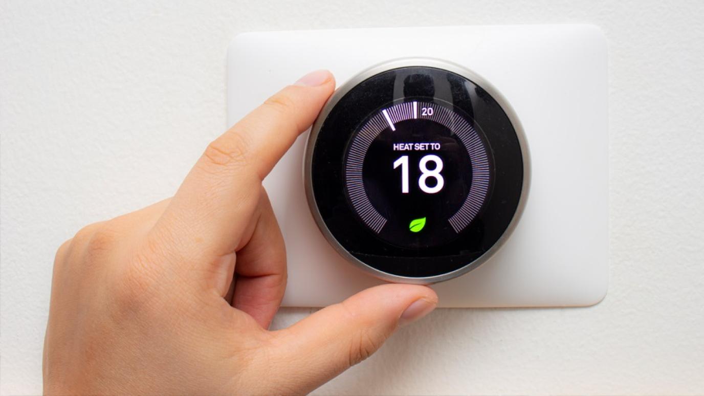 Hand turning the dial on a smart home thermostat that reads 18 degrees