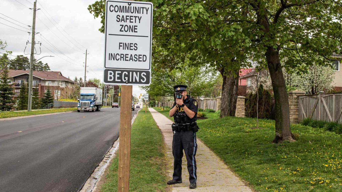 Police Officer standing next to a Community Safety Zone sign with a speed radar in hand