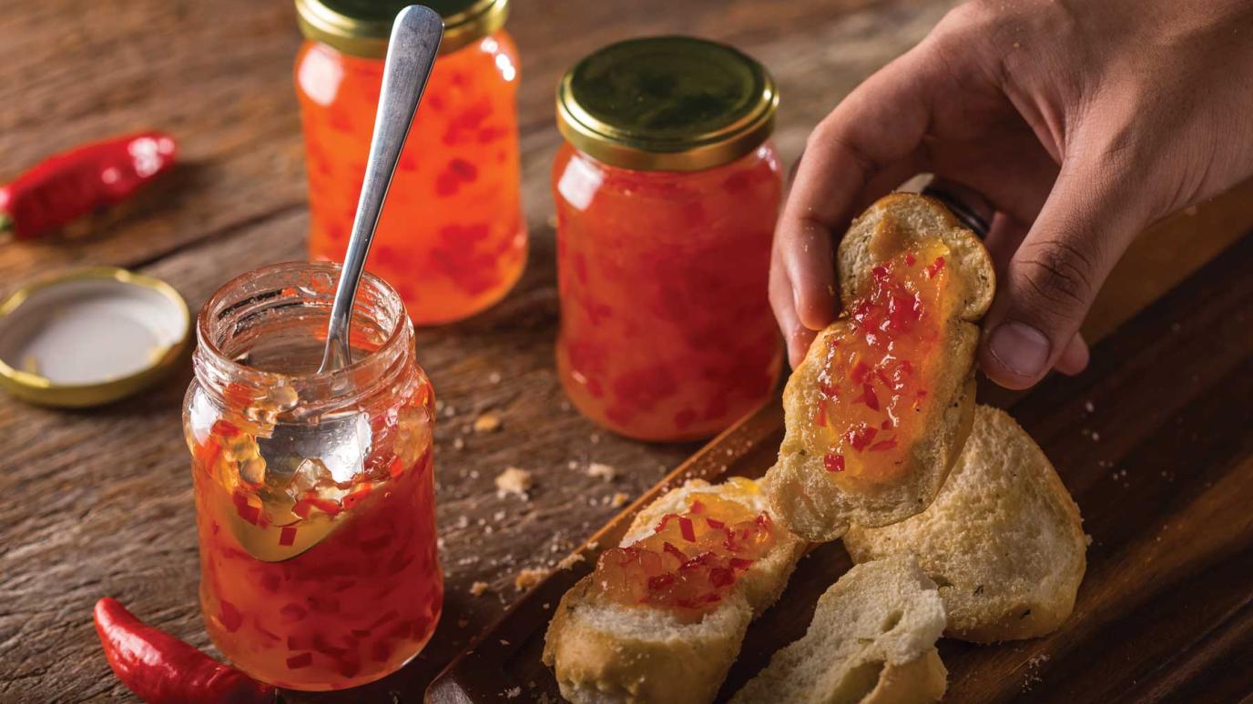 jar of red pepper jelly with spoon and hand holding bread