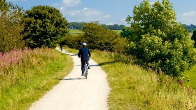 Back view of a cyclist on a gravel pathway through a rural area