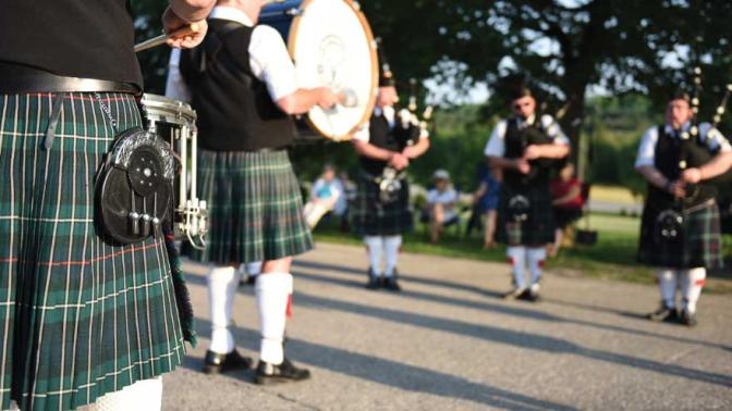 Scottish musicians wearing green plaid kilts playing drums and bag pipes