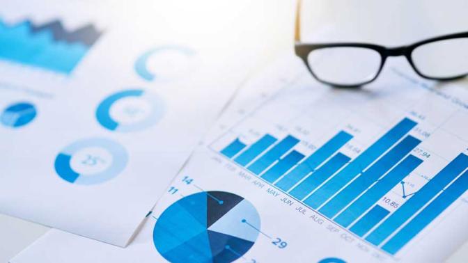 Papers of charts and graphs sitting on a desk next to a pair of glasses