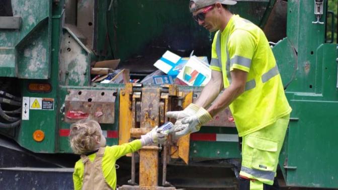 Little boy passes a garbage truck driver a cold drink in appreciation