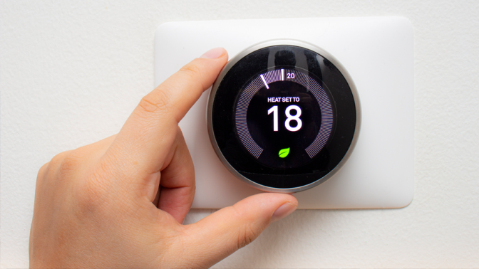 Hand turning the dial on a smart home thermostat that reads 18 degrees