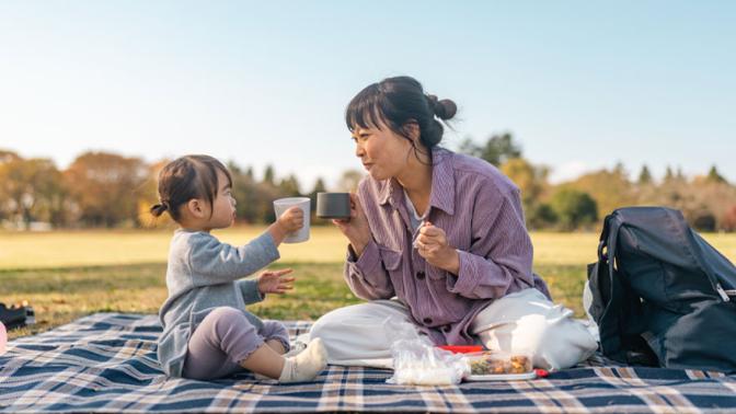 Mom and child cheers their mugs while enjoying a picnic in a rural setting