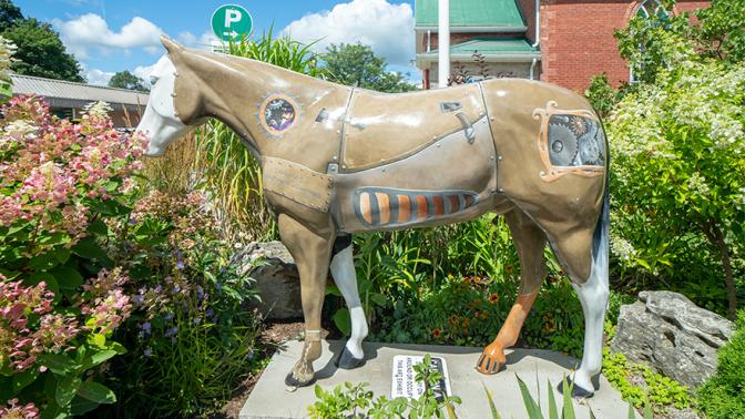 Horse statue on pedestal in rural park surrounded by greenery.