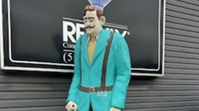 statue of tall man in teal jacket and black pants standing outside