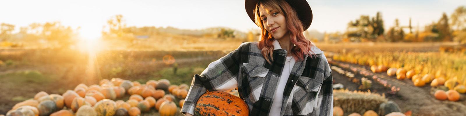 A portrait of a beautiful woman with a pumpkin in her hands on farm at harvesting at sunset in autumn