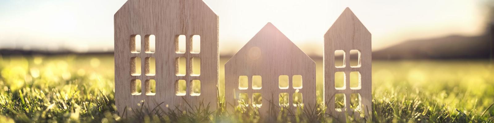 Cut out wooden houses sitting in the grass with sunlight shining through