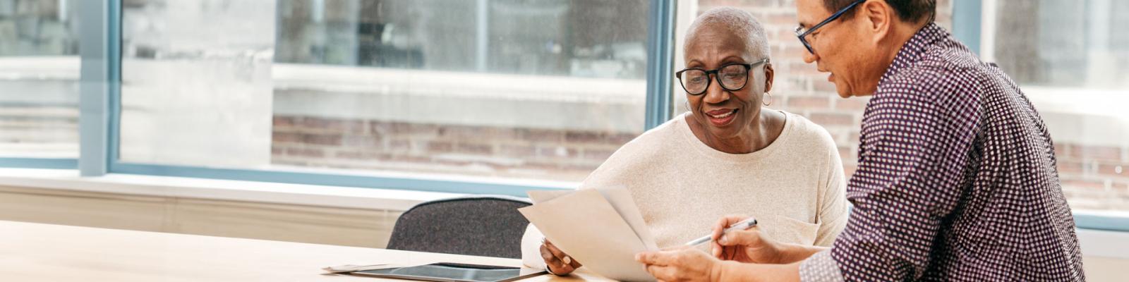 Man reviewing documents with an older woman and offering guidance in an office setting. 