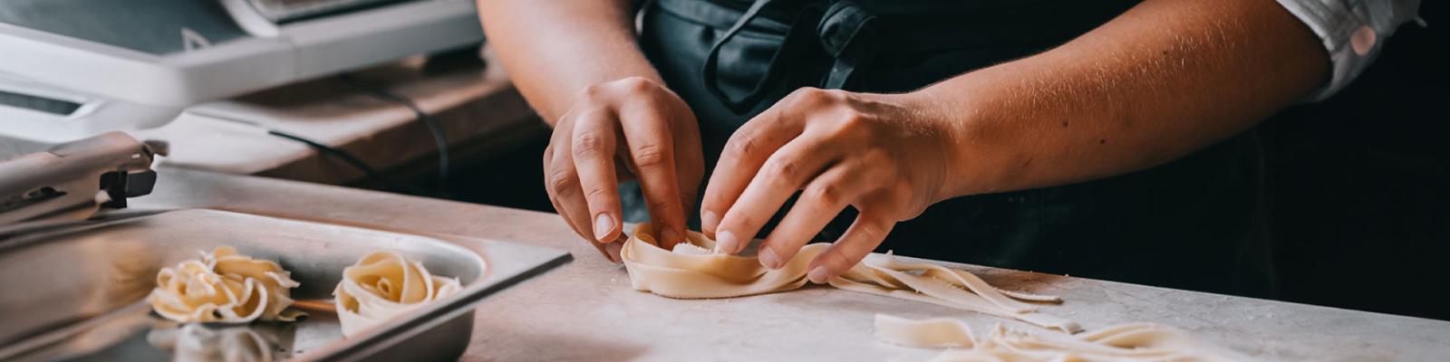 Chef woman's hands making tagliatelle pasta