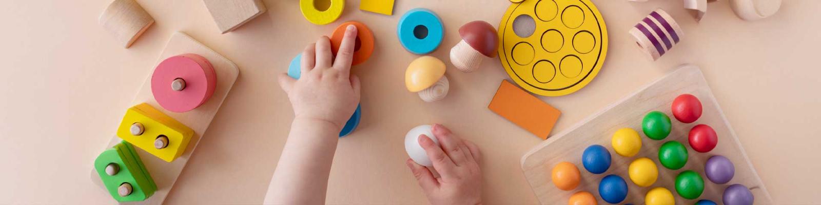 Small toddler hands reach for stacking rings and blocks on a table viewed from above