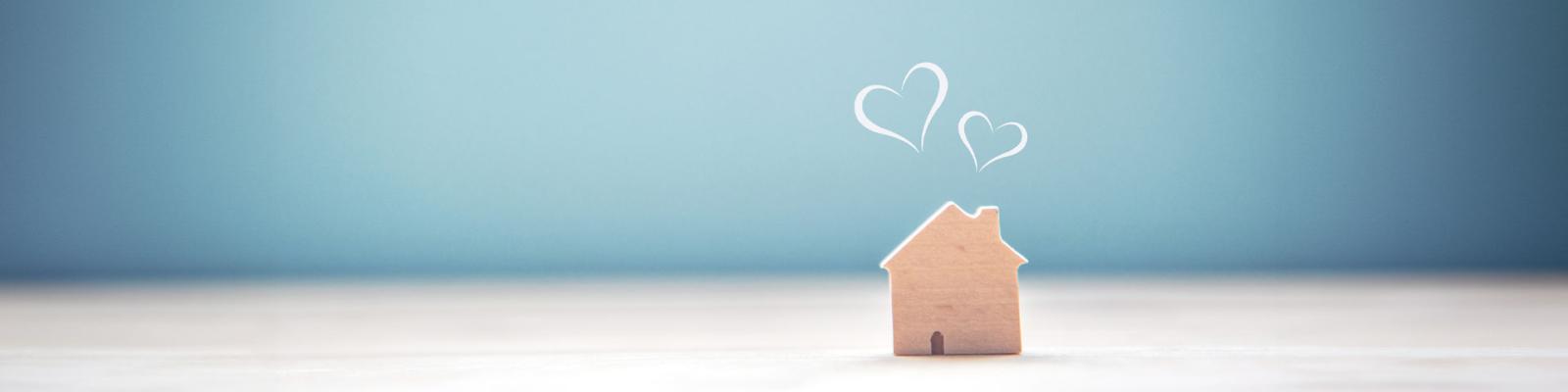 Small wooden house with heart shapes coming out of the chimney on a blue background