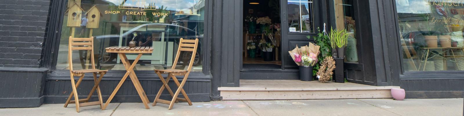 Welcoming store front with a table and chairs in a sunny spot outside the front window.