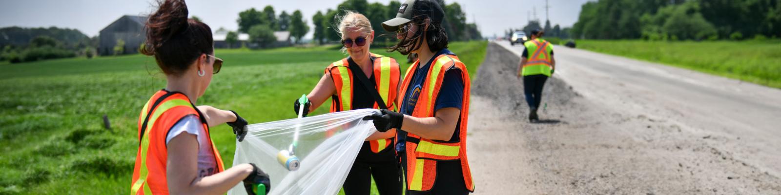 Employess in safety vests pick up garbage at the side of the road as part of Public Works Week