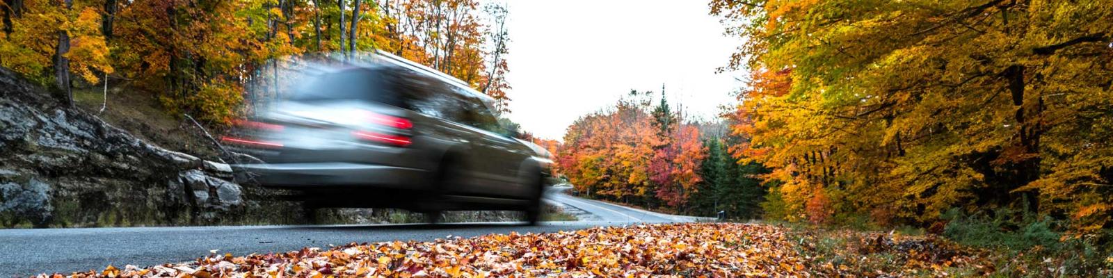 Speeding car down a rural road in the Autumn stirring up leaves as it rounds a corner