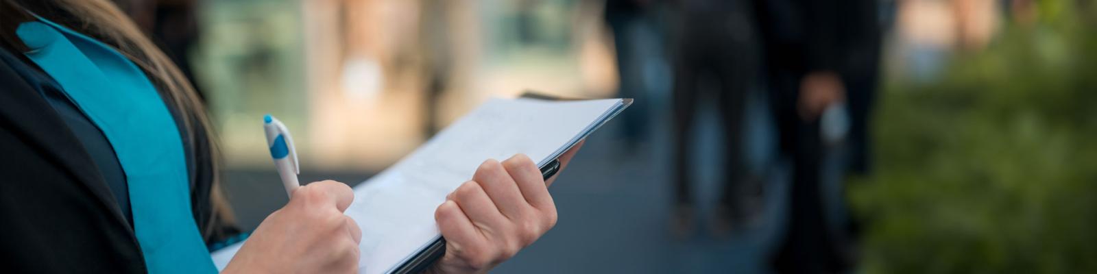 A close up of a woman holding a clipboard outside.