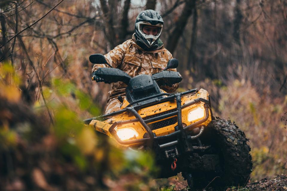 A person in camo drives on an ATV through a forest. 
