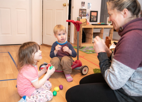 Home childcare provider playing with toy eggs with two young children.