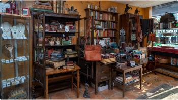 Photograph of three tall and very full bookshelves in an orange room, showcasing a variety of books and bags in different shapes, sizes, and colours. 