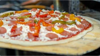 A closeup image of a pizza with pepperoni and green/red/yellow/orange peppers going into a pizza oven.