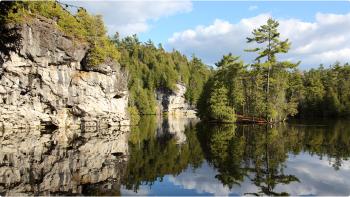 Photo of Rockwood Conservation area showcasing blue skies reflected in the lake, surrounded by large rock formations and green trees. 