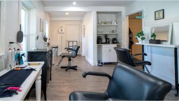 Interior view of a hair salon with three black chairs sitting in front of mirrors surrounded by hair products.