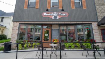 Photograph of the front of a grey building with wooden shutters, the sign above the door reads 'Moorefield Diner' above a coffee cup.