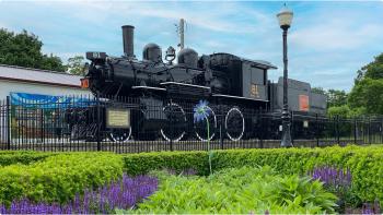 Historic black train engine sits on display next to floral gardens