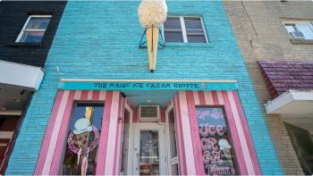 A bright blue painted brick building with pink and white strips around the store entrance. A scultpure of an ice cream cone hangs above the door.