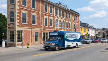 Image of a blue bus parked in front of a three-story red brick building with arched windows. 