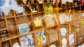 Close-up image of a framed wooden printer’s tray full of various antique stamps and colourful trinkets.