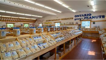 The interior of a store with rows of wooden bins full of packaged peanuts and large text on the white walls that reads ‘Ontario Grown Peanuts’ in navy blue lettering. 