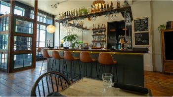 Image of a well-light restaurant with a tall green bar surrounded by liquor bottles and glassware, with five brown leather chairs pulled up to the counter.