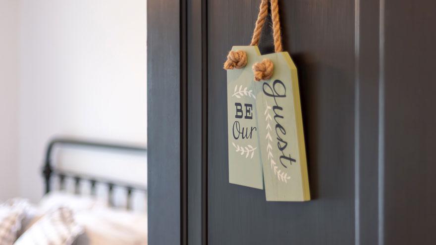 Guest bedroom with an open door and sign that says "Be our guest"