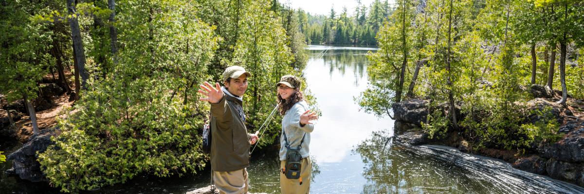 two people waving from a cliff with fishing rods