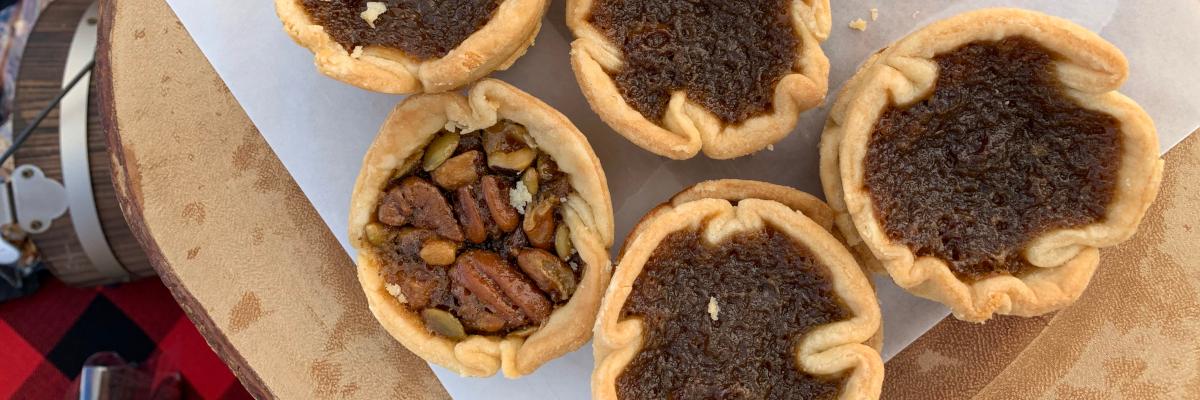 An overhead shot of several butter tarts, with one filled with pecans, on a wooden board
